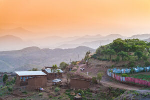Rural village with one person walking in distance next to a red and blue fence between houses at sunset Lalibela Ethiopia Horn of Africa
