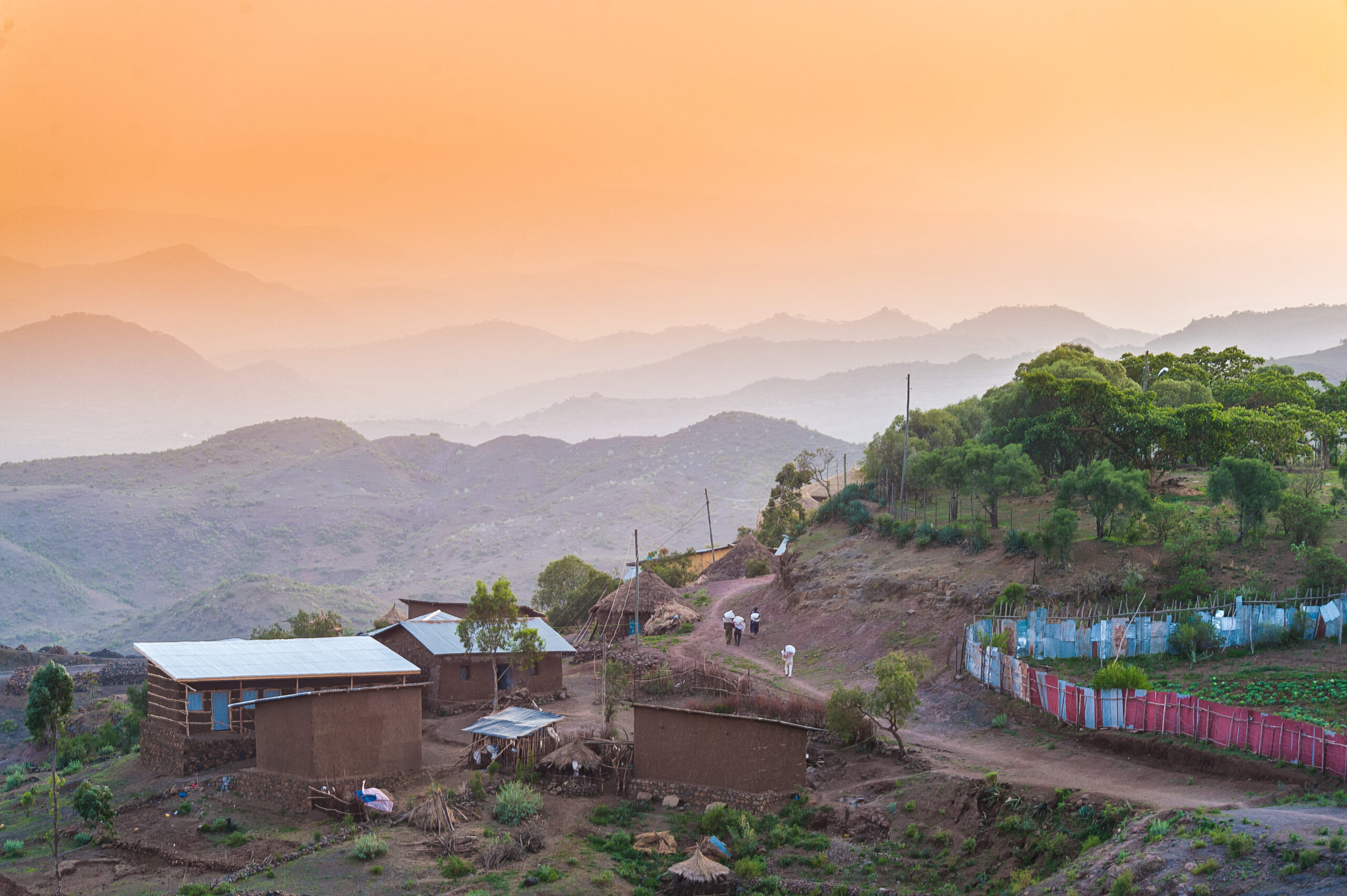 Rural village with one person walking in distance next to a red and blue fence between houses at sunset Lalibela Ethiopia Horn of Africa