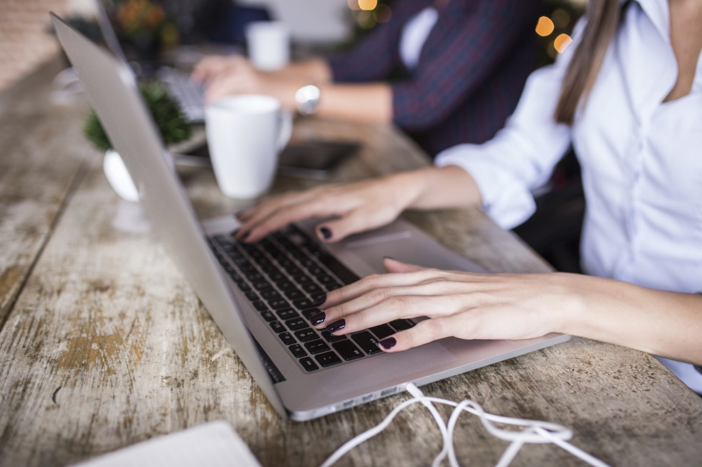 Young woman using laptop at home office. Modern office interior, wooden table, close up of her hands